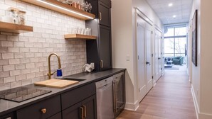 A modern kitchen with dark cabinetry, a stainless steel dishwasher, and a wooden countertop. - Modern Luxury in Downtown TC (Traverse City)