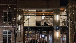 A modern building with large windows and a glass facade, featuring several businesses including a restaurant and a coffee shop. - Modern Luxury in Downtown TC (Traverse City)