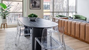A modern living room with a round dining table, clear chairs, a green sofa, and a large window offering a city view. - Modern Luxury in Downtown TC (Traverse City)