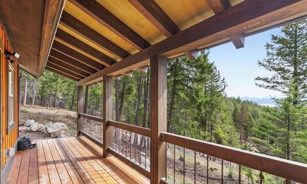 A wooden deck with a railing, overlooking a forested area with trees and a mountain in the distance.
