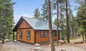 A cabin with a sloped roof, wooden exterior, and a gravel driveway surrounded by trees.
