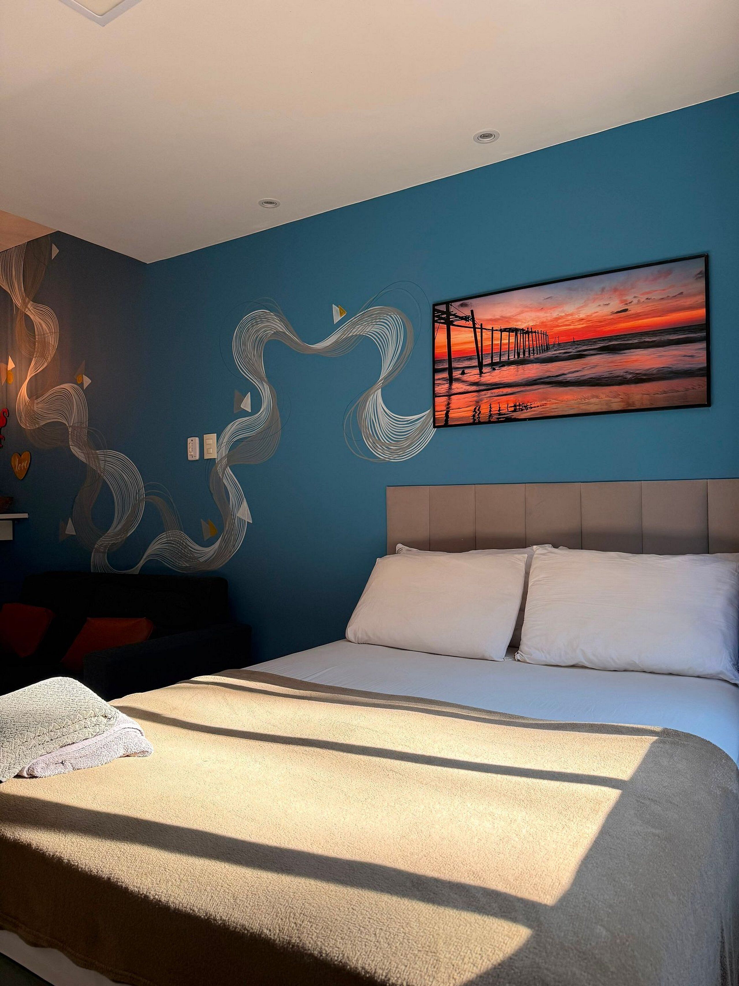 A bedroom with a bed, a wall painting, and abstract wall art.