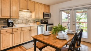 A kitchen with wooden cabinets, a stone backsplash, a coffee maker, a microwave, and a dishwasher. - Compass Cottage (St. Augustine)