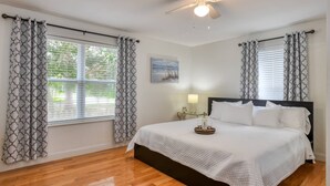 A bedroom with a bed, a ceiling fan, and a window with curtains. - Compass Cottage (St. Augustine)