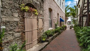 A narrow brick pathway flanked by historic buildings with wooden shutters and potted plants. - Compass Cottage (St. Augustine)