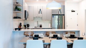 Uma cozinha moderna com uma ilha central, eletrodomésticos de aço inoxidável e uma área de jantar com cadeiras brancas.