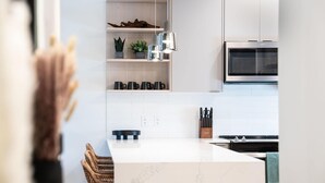 Uma cozinha moderna com armários brancos, forno embutido e uma ilha central com bancada de mármore.
