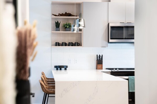 Una cocina moderna con armarios blancos, horno empotrado e isla central con encimera de mármol.