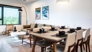 Uma sala de jantar moderna com uma mesa posta para quatro pessoas, um sofá, uma mesa de centro e uma janela grande.