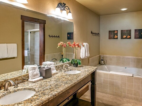 Un baño con encimera de granito, dos lavabos, un espejo grande, una ducha y una bañera.