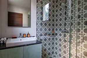 A modern bathroom with a large sink, mirror, and shower with a geometric tile pattern.