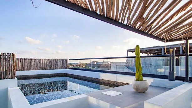 A rooftop pool area with a modern design, including a geometric pool, a cactus plant, and a wooden pergola. - Kite Suite 207 (Tulum)