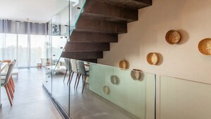 A modern interior with a glass staircase, a dining area with chairs, and decorative wall plates. - Kite Suite 207 (Tulum)