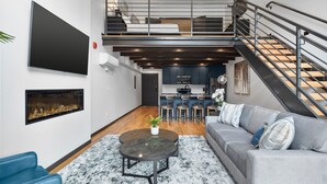 Ein moderner Wohnbereich mit Sofa, Couchtisch, Kamin, Küchenzeile und einer Treppe.
