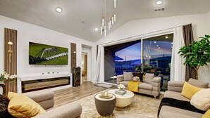 A modern living room with a flat-screen TV, comfortable sofas, a coffee table, and a large window offering a view of the outdoors. - New Large Home-Views-Mountain, Lake & Golf (Indio)