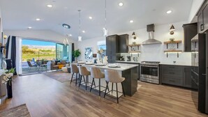 A modern kitchen with a central island, stainless steel appliances, and a dining area with bar stools. - New Large Home-Views-Mountain, Lake & Golf (Indio)