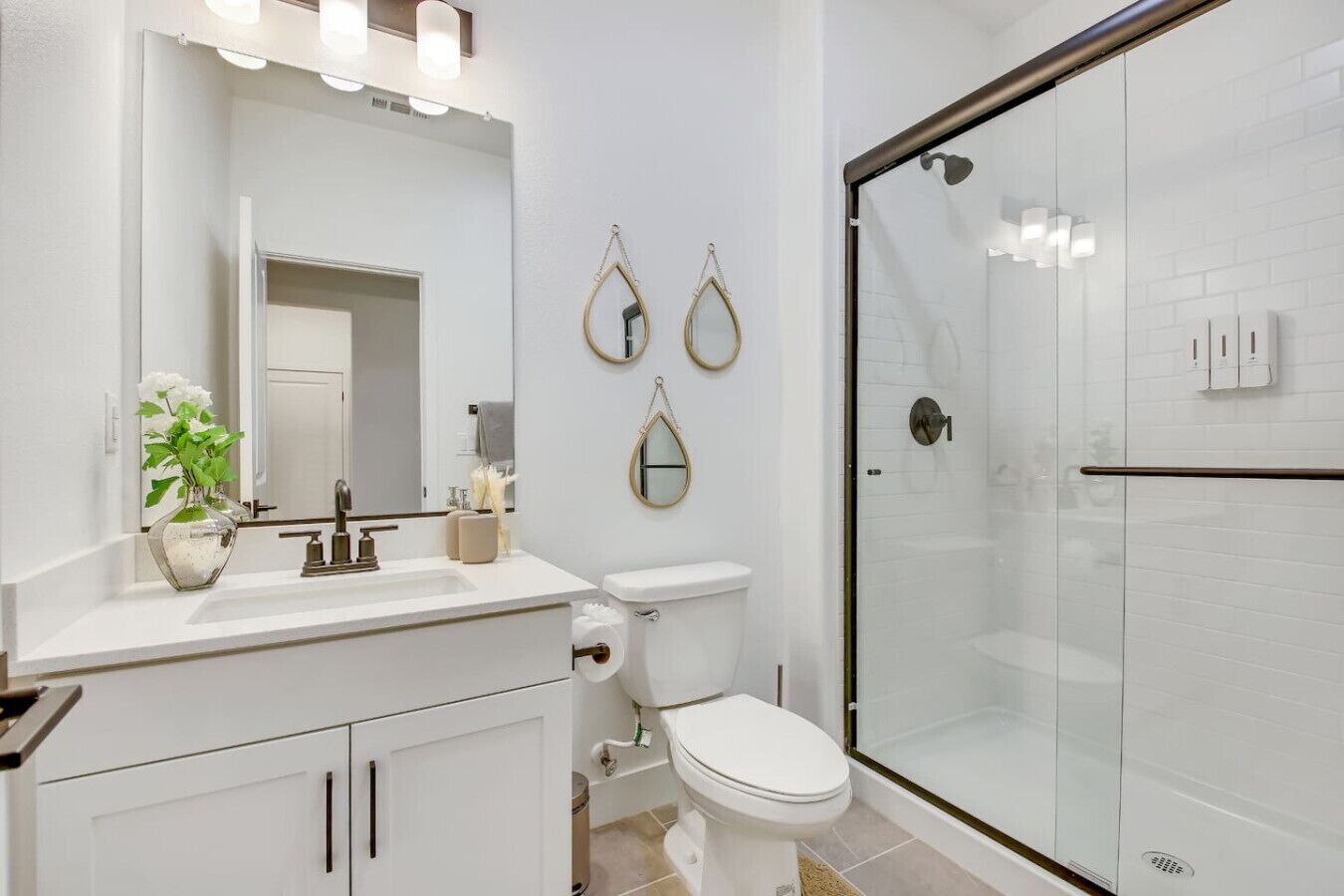 A modern bathroom with a glass shower enclosure, a white sink with a mirror above, and decorative wall mirrors.