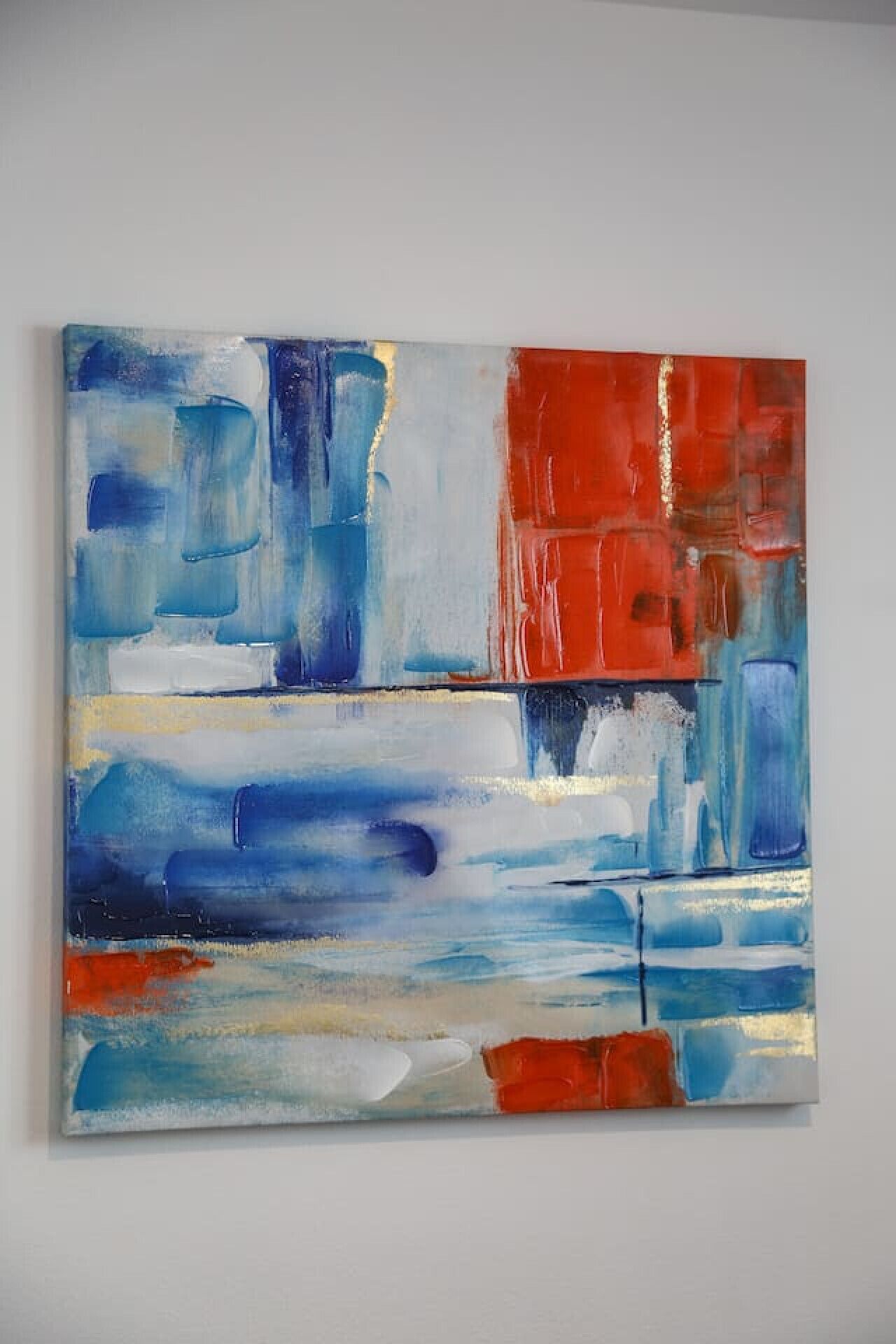 A large abstract painting with blue, red, and white colors on a white wall.