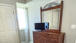 Un dormitorio con una cama grande, un aparador de madera, un televisor de pantalla plana y un espejo sobre el aparador.