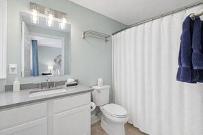 A bathroom with a sink, mirror, toilet, and shower curtain.