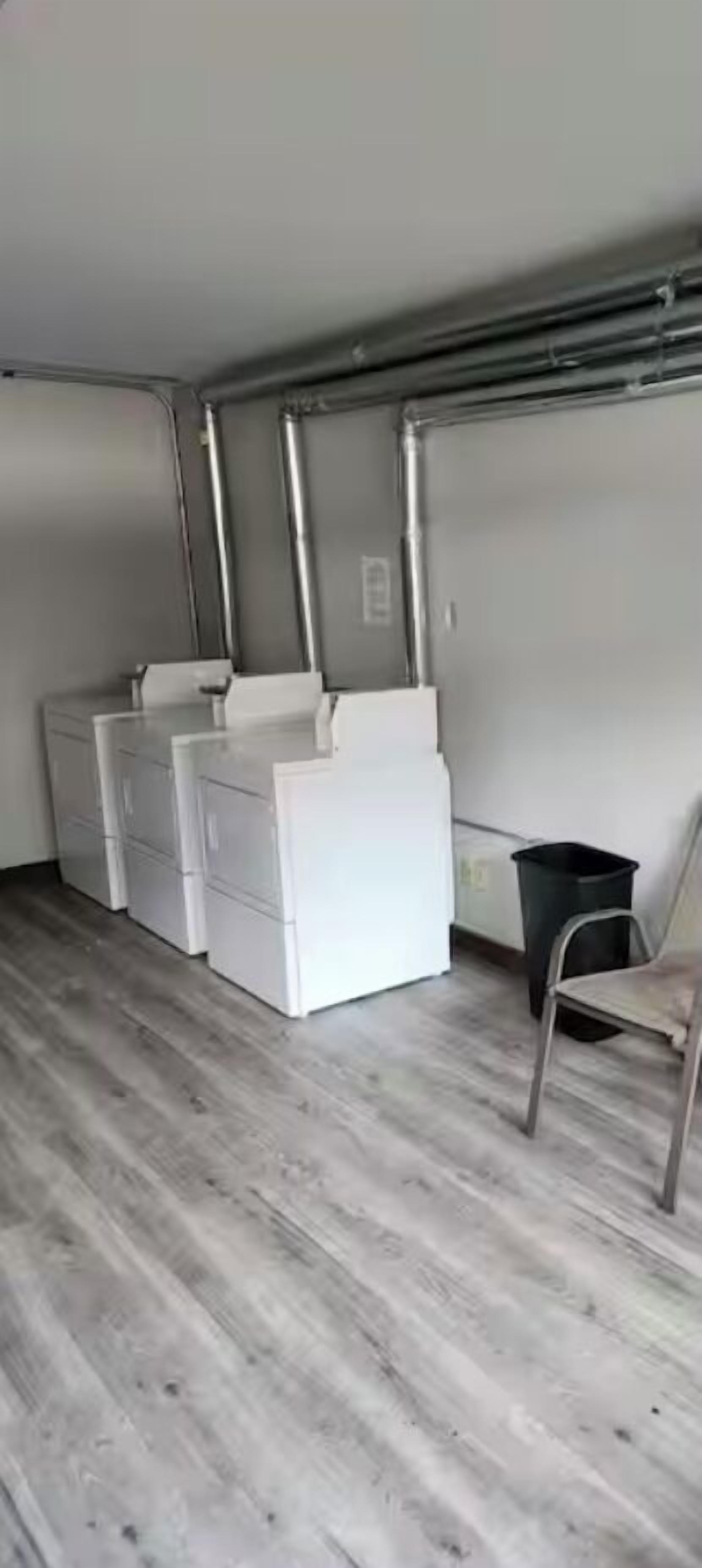 A compact room with a wooden floor, white storage units, a trash bin, and a chair.