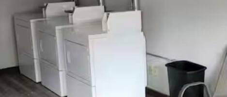 Una habitación compacta con suelo de madera, muebles de almacenamiento blancos, un cubo de basura y una silla.