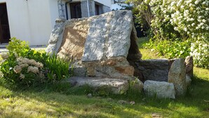 A stone structure with a partially collapsed wall, surrounded by grass and flowering plants. - Joli Cottage en Pierres Debouts Dans un Beau Jardin Fleuri Proche Plage (Nevez)