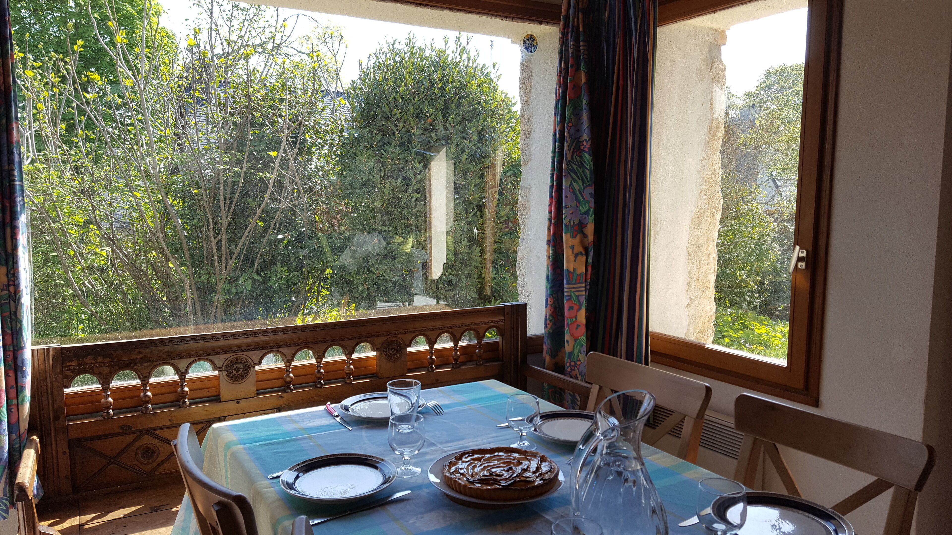 A dining table set with plates, glasses, and a cake, overlooking a garden with trees and a stone structure.