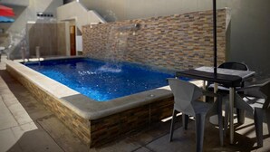 Uma piscina com muro de tijolos, uma mesa e cadeiras.