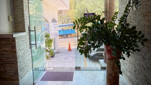 Entrada de hotel com porta de vidro, um vaso de planta e uma placa indicando a saída.