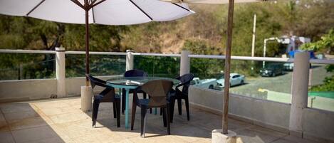 Een terras buiten met een tafel, stoelen, een grote parasol en uitzicht op de parkeerplaats.