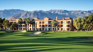 Ein Hotel mit Golfplatz davor, mit einem großen Gebäude, mehreren Balkonen und Palmen.