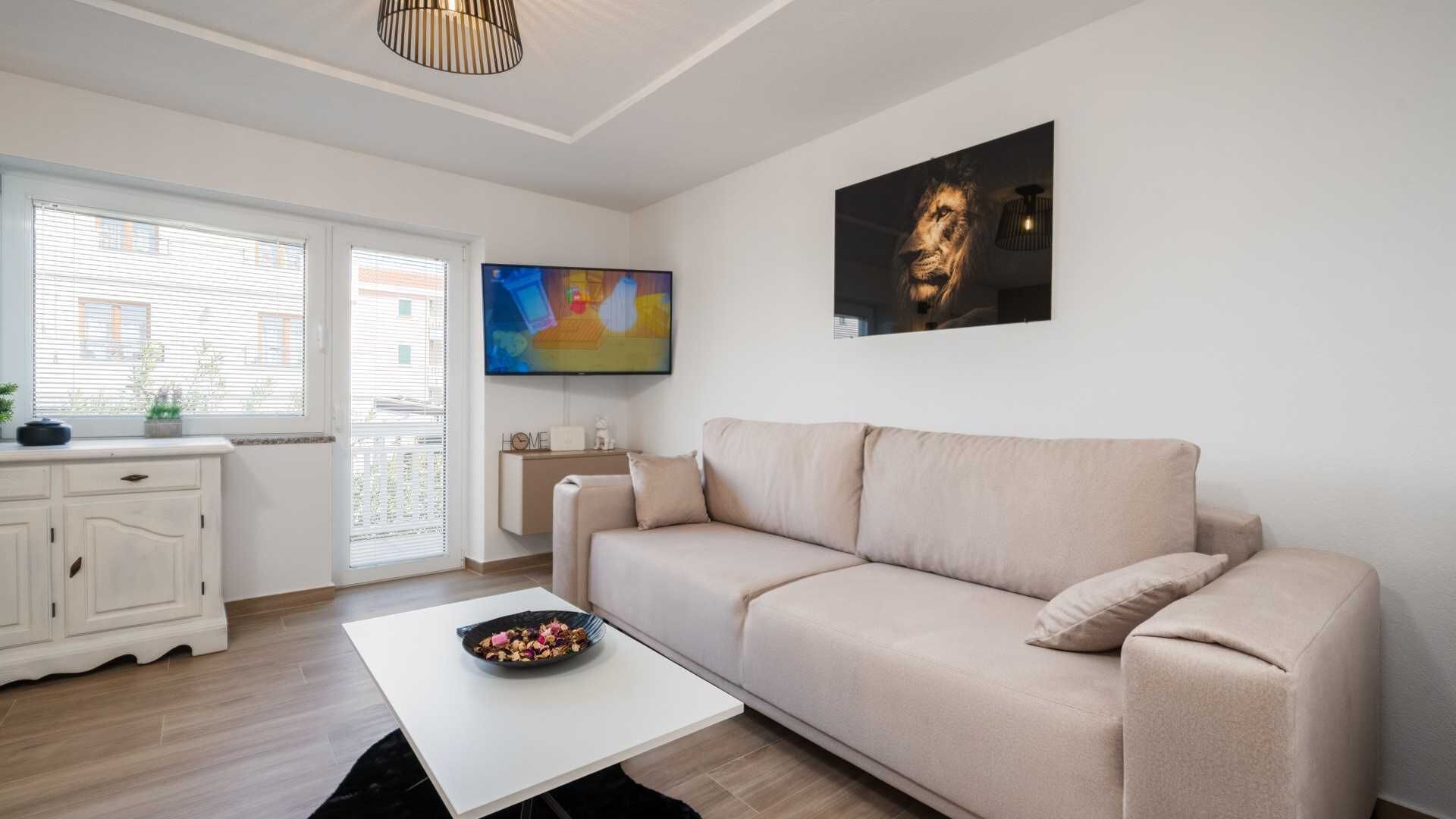 A modern living room with a beige sofa, a white coffee table, and a flat-screen TV.