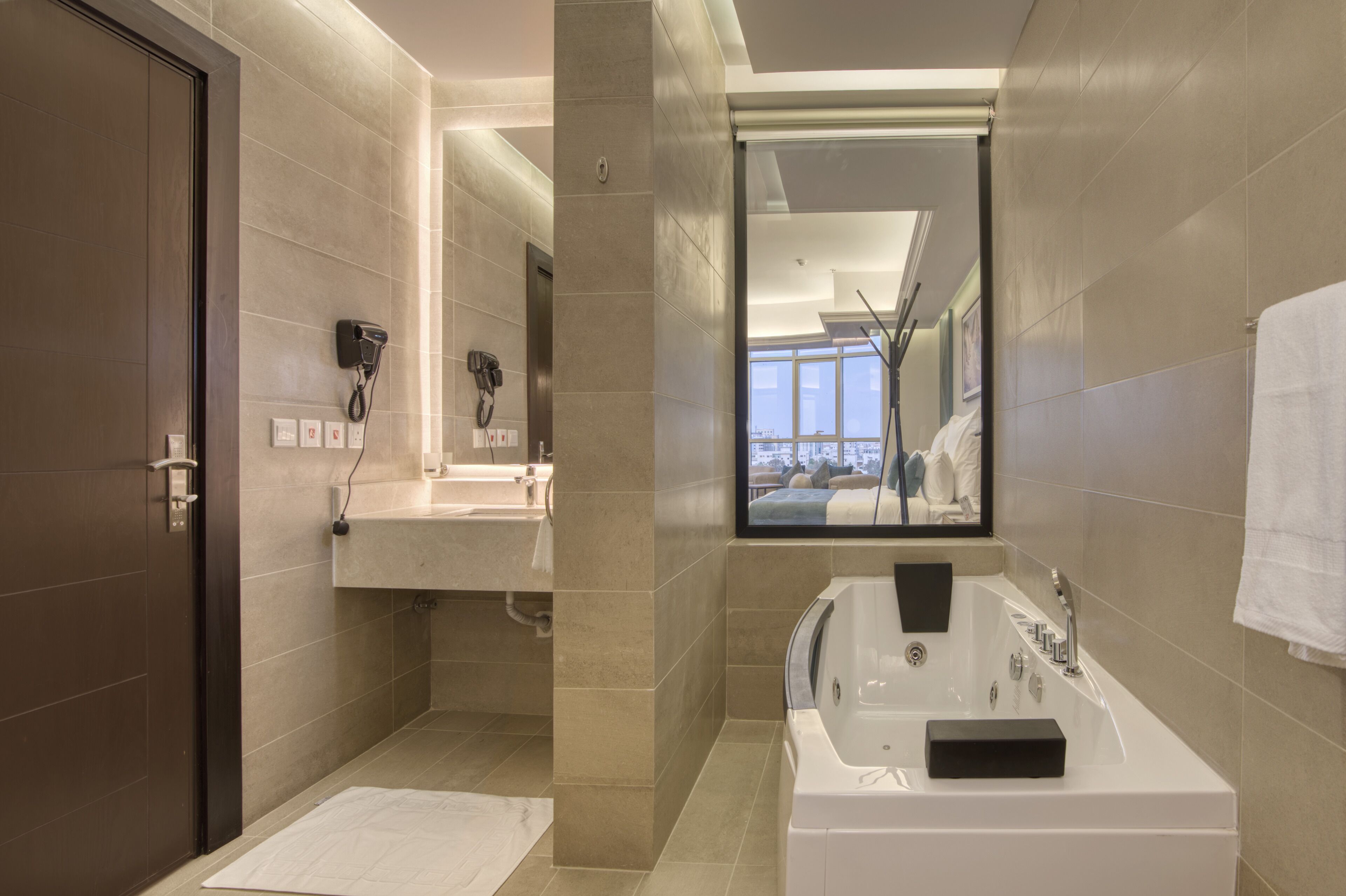 A modern bathroom with a large bathtub, a vanity with a mirror, and a hairdryer mounted on the wall.