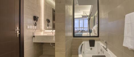 A modern bathroom with a large bathtub, a vanity with a mirror, and a hairdryer mounted on the wall.
