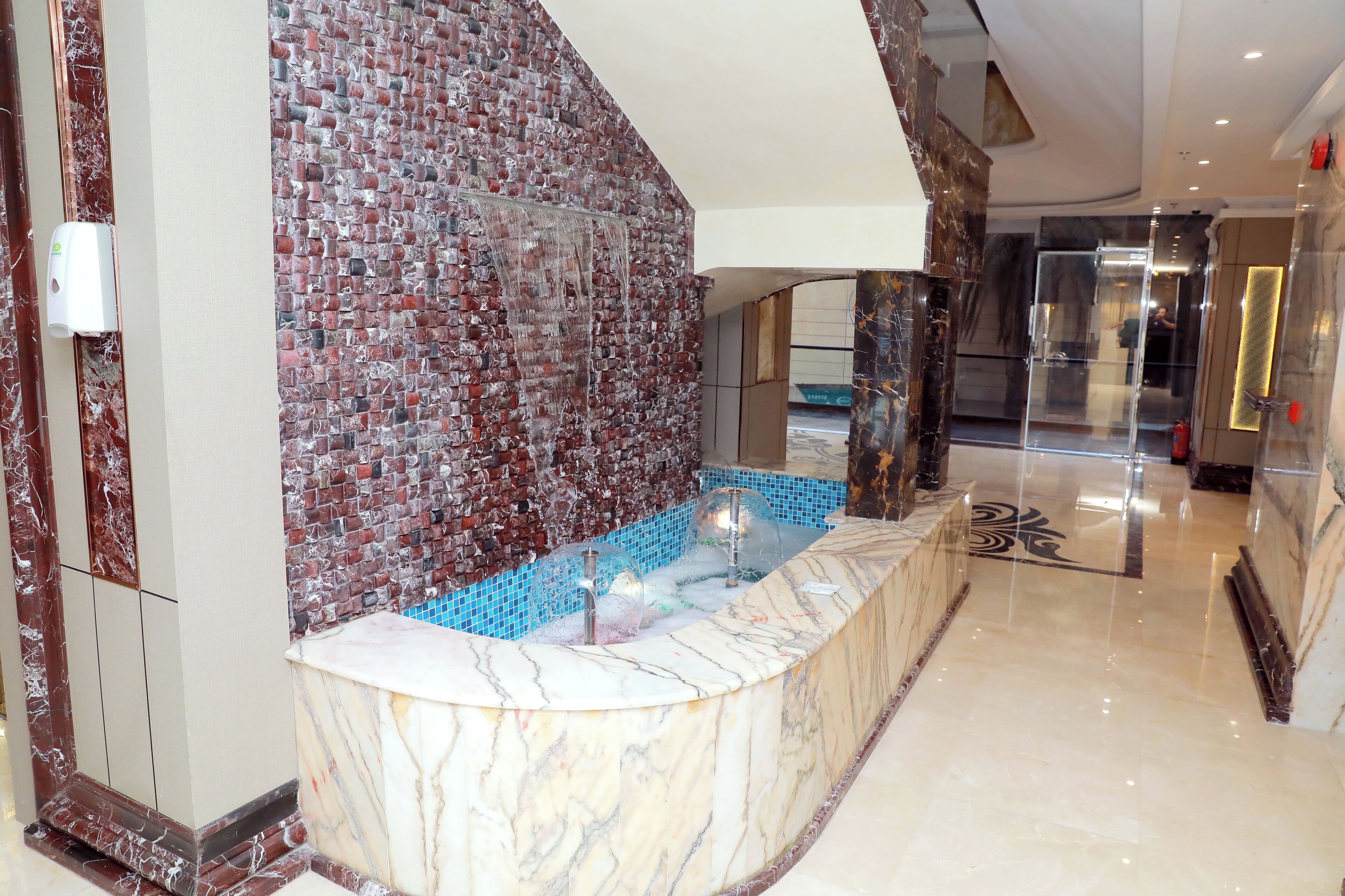Un área de recepción de mármol con un separador de vidrio, una pared de azulejos y un box de ducha de vidrio transparente al fondo.