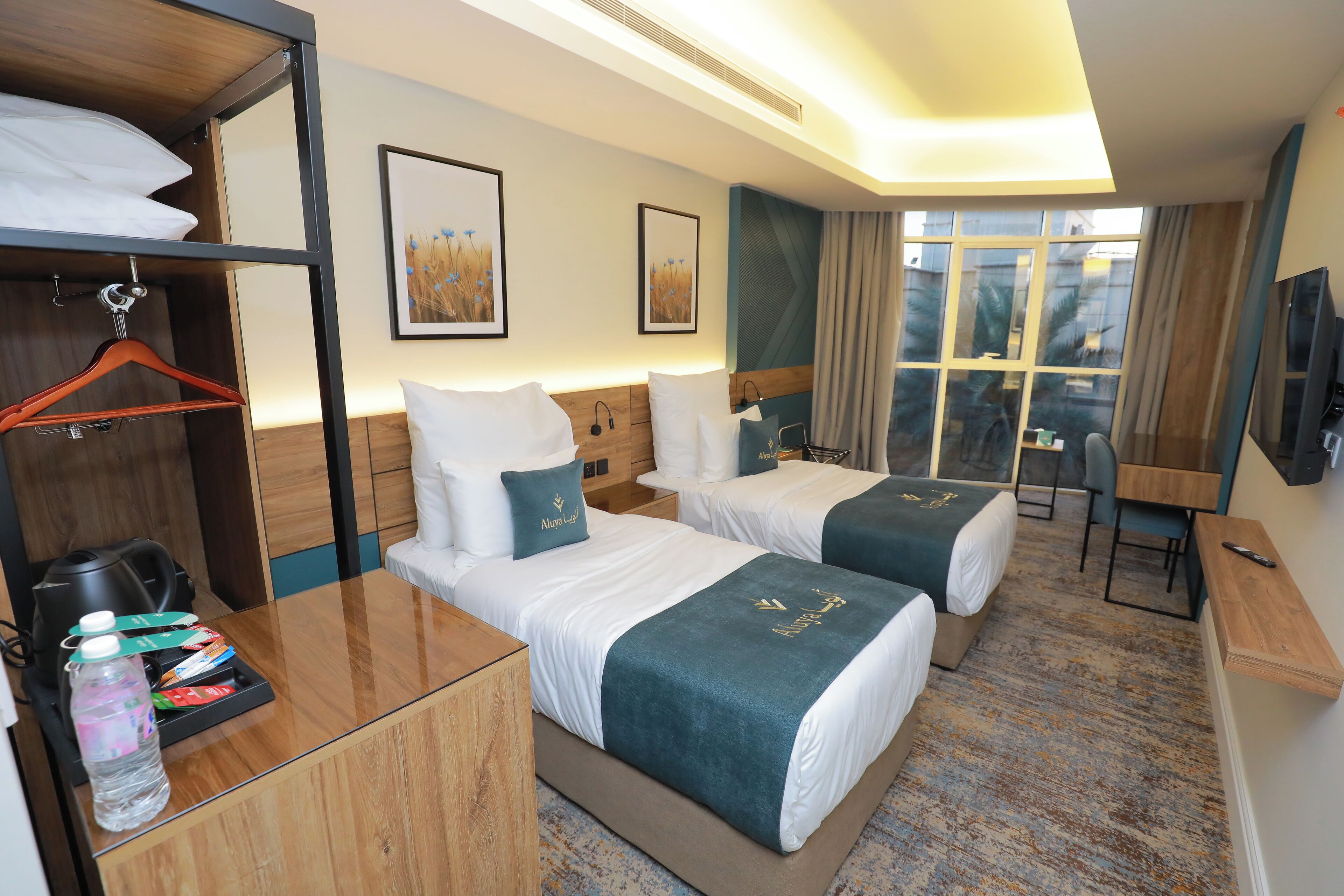 Een hotelkamer met twee bedden, een bureau, een stoel, een televisie en een raam met gordijnen.