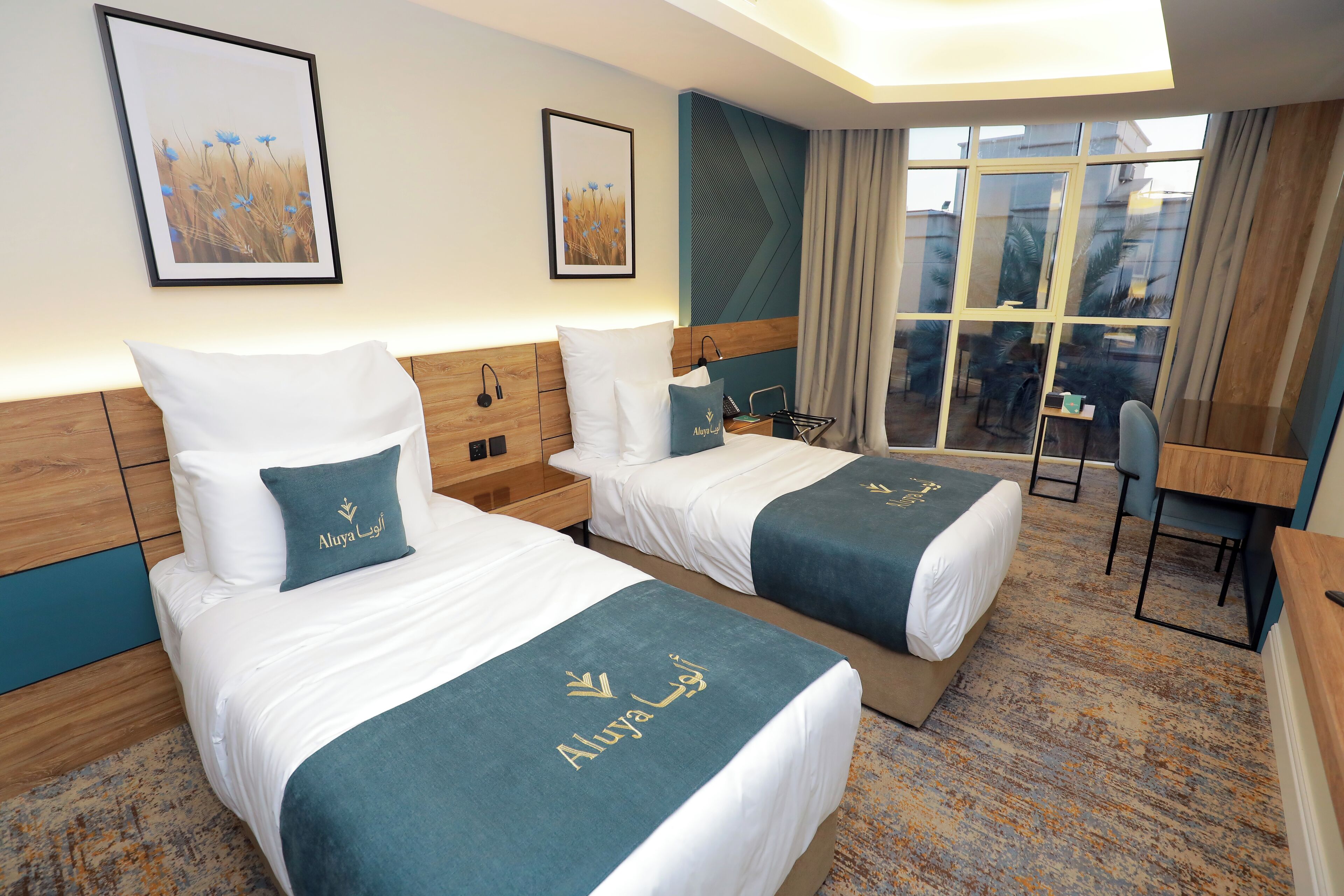 A hotel room with two beds, a desk, a chair, and a large window.
