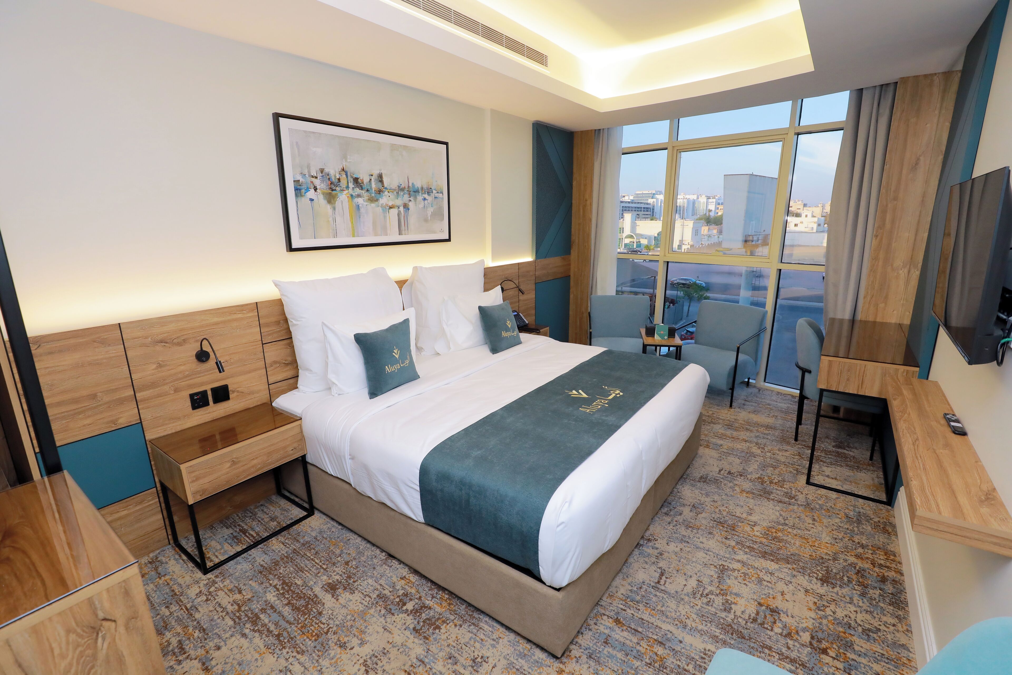 Habitación de hotel moderna con una cama grande, un escritorio, una silla y un ventanal que ofrece vistas de la ciudad.