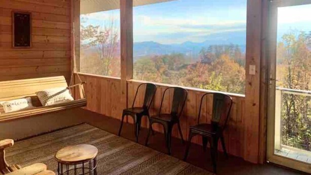 A wooden cabin with a balcony, a bed, and a view of a mountainous landscape.