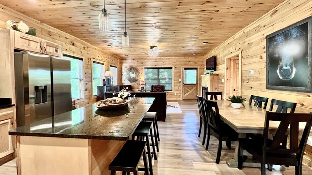 A modern kitchen with a central island, wooden cabinetry, and a dining area with a large table and chairs.