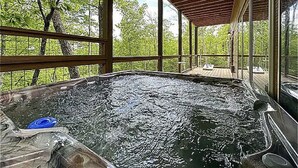 A hot tub area with a wooden deck and large windows overlooking a forest.