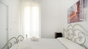 Un dormitorio con cama, cortinas, una mesita de noche y un cuadro colgado en la pared.