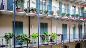 Un edificio de varios pisos con balcones, cada uno adornado con plantas en macetas y contraventanas azules.
