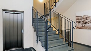 Una escalera con barandilla metálica, una puerta con un letrero y una pared con una fotografía.