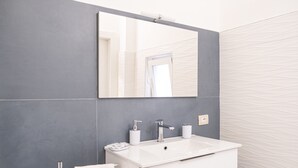 A modern bathroom with a white vanity, a large mirror, and a grey tiled wall. - Sun&Moon Apartment (Bari)