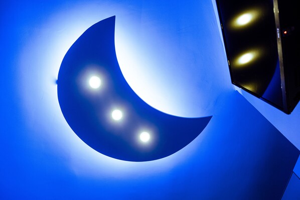 Lámpara en forma de luna creciente con tres bombillas sobre una pared azul.