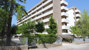 A multi-story residential building with balconies, surrounded by trees and a fenced area. - Luminous Apartment Just Next to the Beach (San Michele al Tagliamento)
