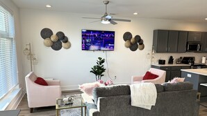 Una sala de estar moderna con un sofá gris, dos sillones, una mesa de centro de vidrio y un televisor montado en la pared.