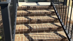 Un juego de escalones de ladrillo al aire libre que lleva a una puerta verde con un letrero de número encima.